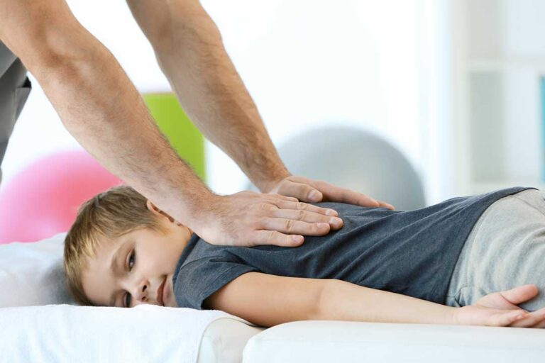 Person seated at home gently icing a swollen knee beside a chair and exercise mat.
